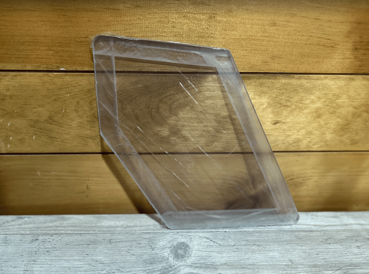Clear polycarbonate Case and New Holland skid steer kick window leaning against a wood plank surface