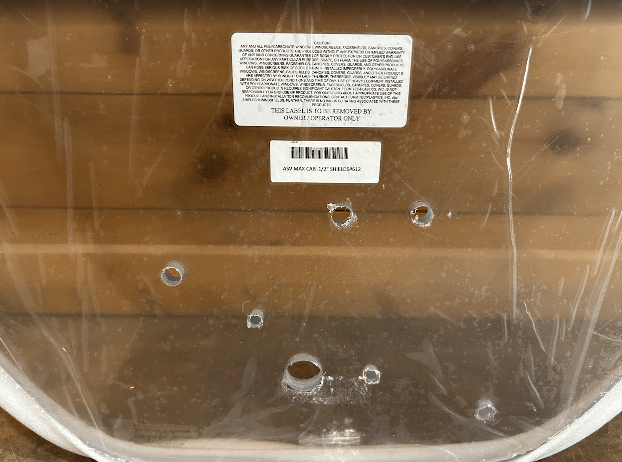 Bottom view of ASV Max-Series polycarbonate windshield showing product barcode label and pre-drilled mounting holes