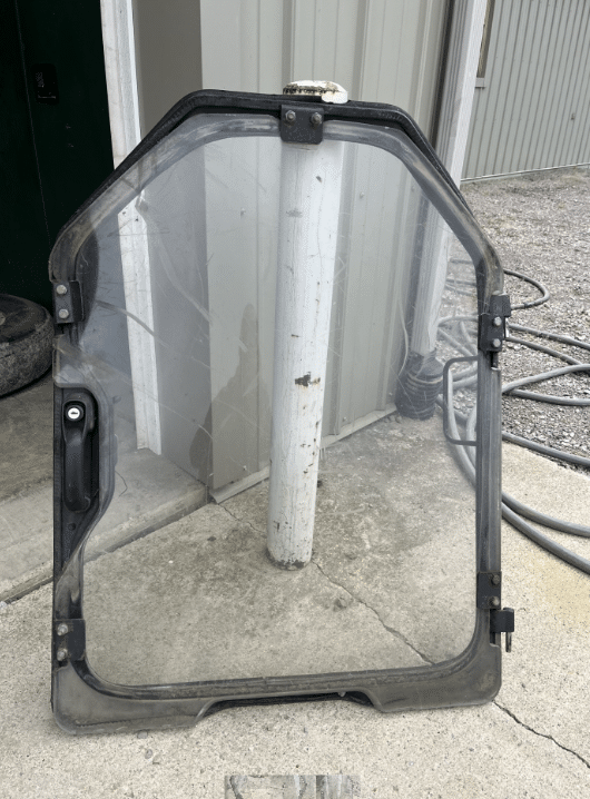 Bobcat D Series Forestry windshield replacement shown with black mounting frame, clear polycarbonate panel and hardware