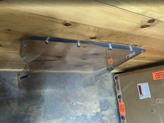 Close-up of top edge of Bobcat G Series laminated forestry windshield showing mounting studs and hardware along the upper frame