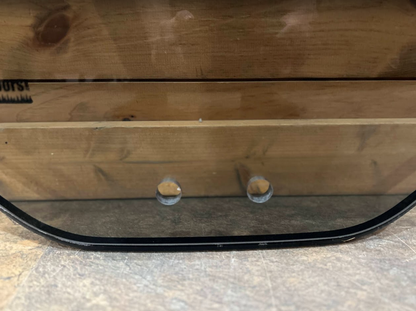 Close-up of bottom edge of Bobcat M Series 2-hole forestry windshield showing the two mounting holes and black rubber door seal