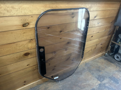 Bobcat M Series 2-hole clear polycarbonate forestry windshield with black door seal frame, angled view showing hinge side and mounting holes