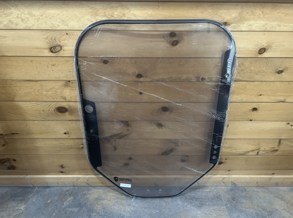 Bobcat M Series 2-hole clear polycarbonate forestry windshield with black door seal frame in protective wrap, front view against wood wall