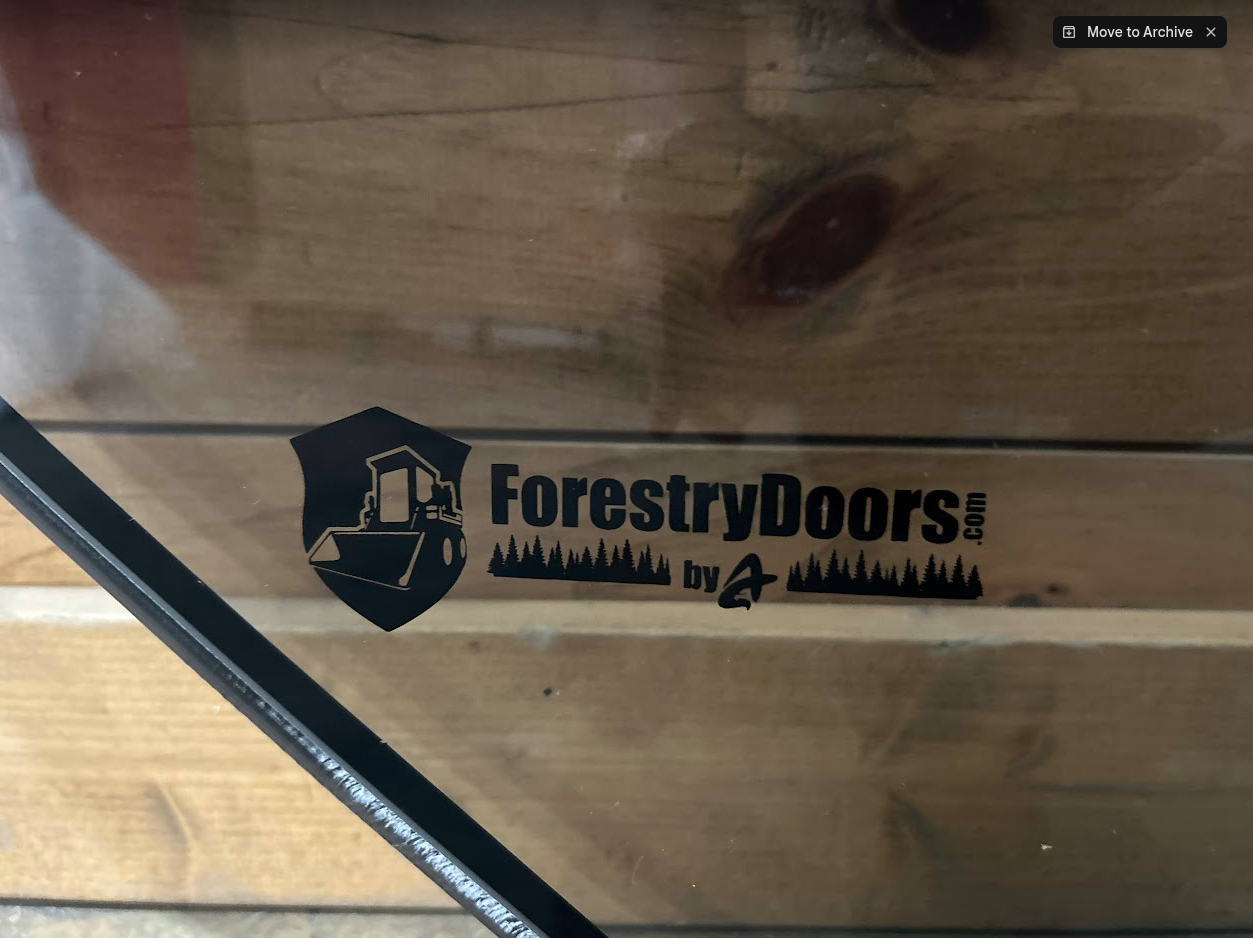 Close-up of ForestryDoors.com brand logo on Bobcat M Series 2-hole forestry windshield with black door seal frame visible