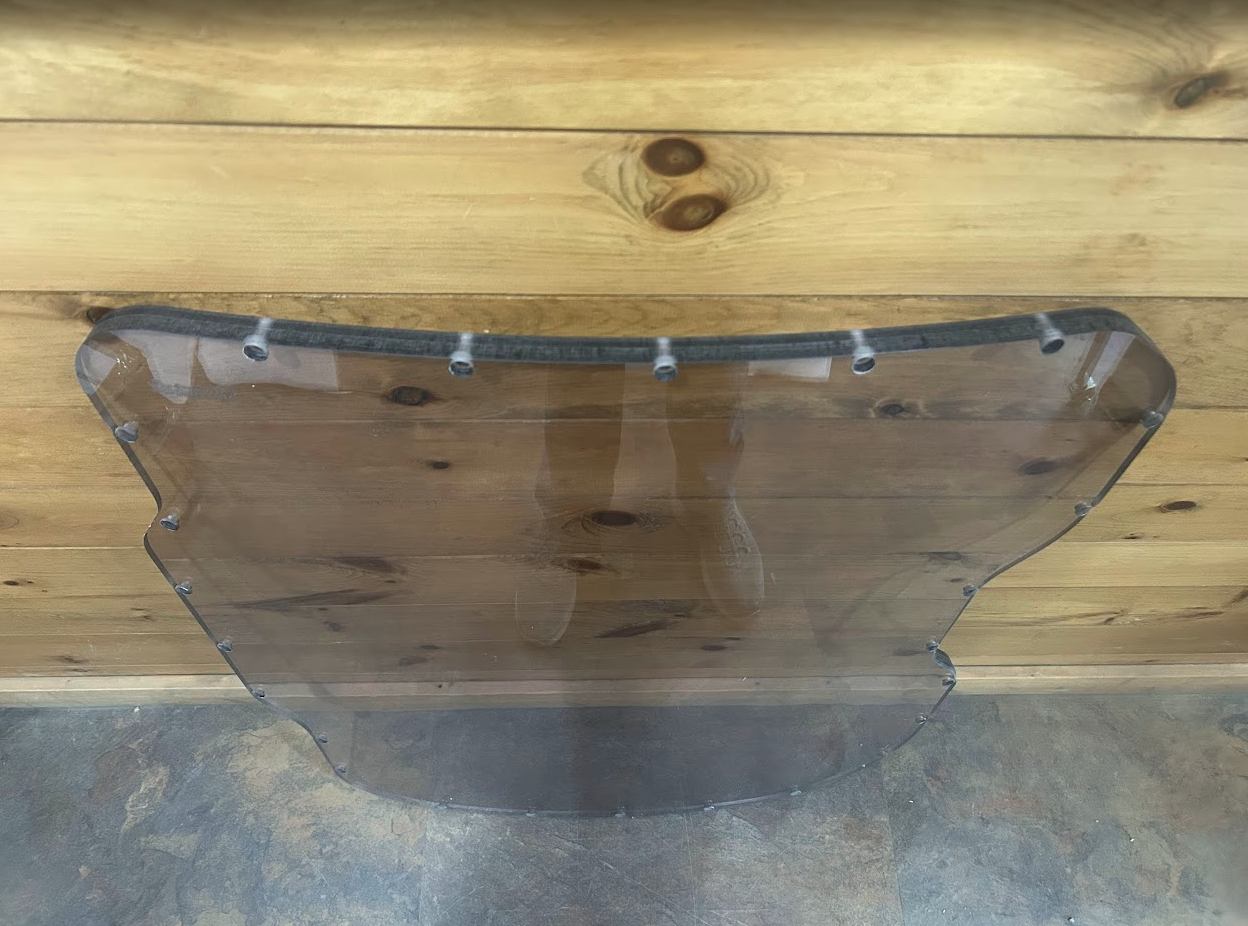 Bobcat M Series 3/4 laminated forestry windshield laid flat showing top rubber seal, mounting bolts, and transparent polycarbonate body