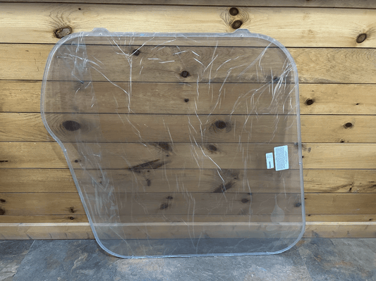Bobcat M Series clear polycarbonate side window replacement with protective film, front view against wood background