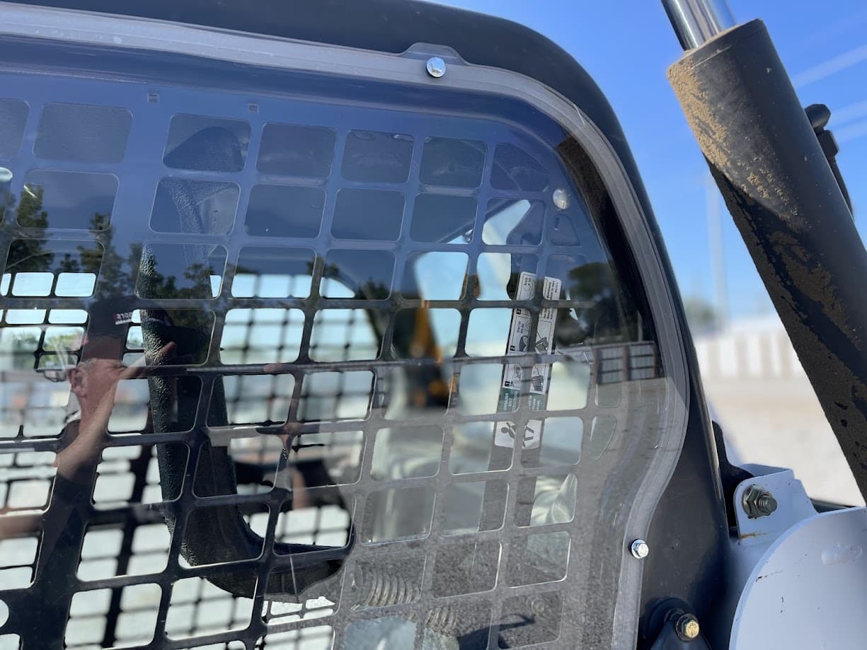 Interior view of Bobcat M Series cab showing polycarbonate side window installed behind mesh guard protection screen