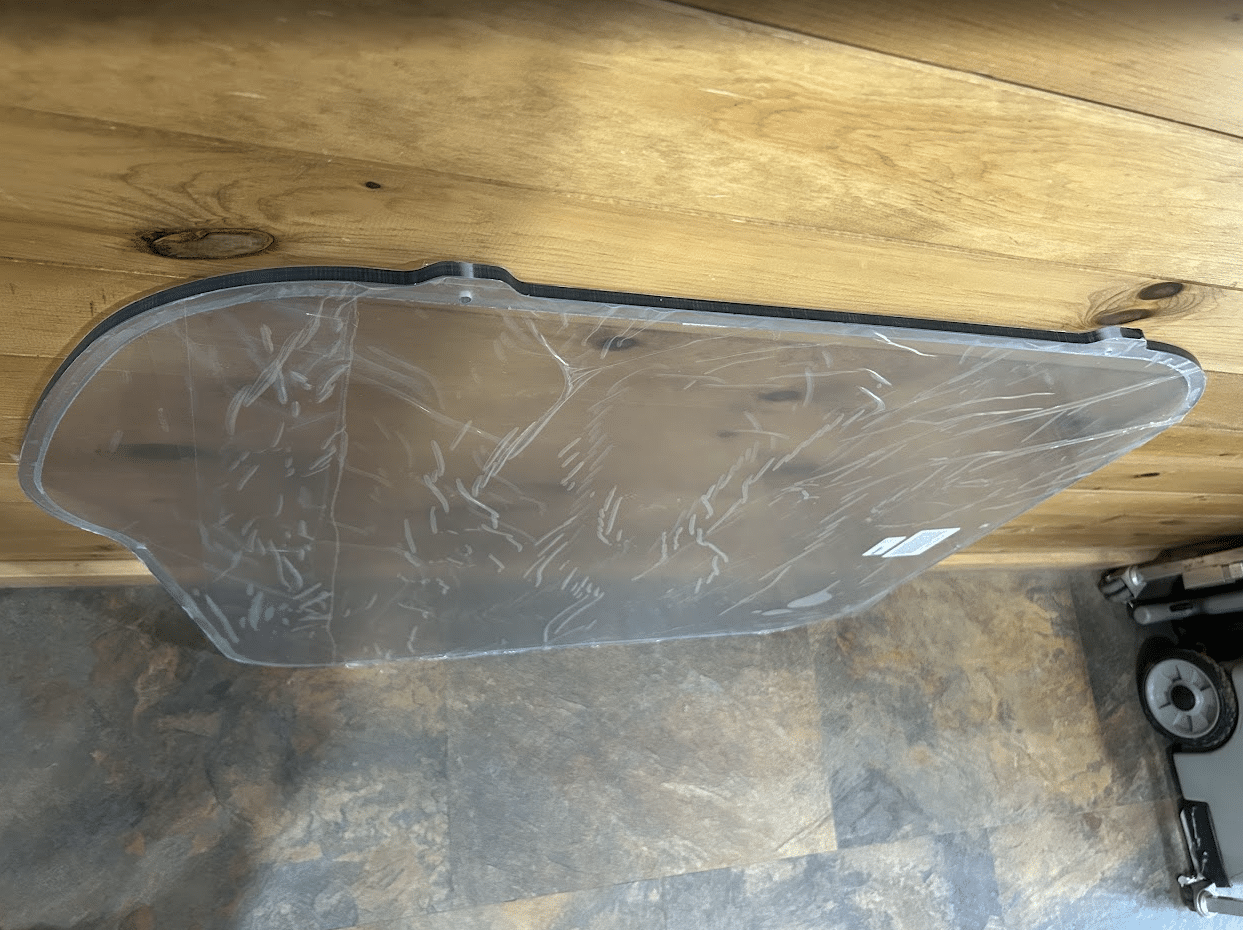 Bobcat M Series polycarbonate side window with protective film, overhead view showing full panel shape and curved cutout