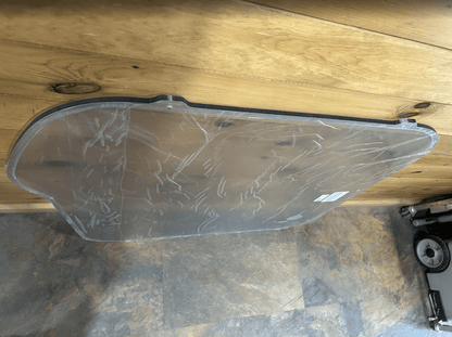 Bobcat M Series polycarbonate side window with protective film, overhead view showing full panel shape and curved cutout