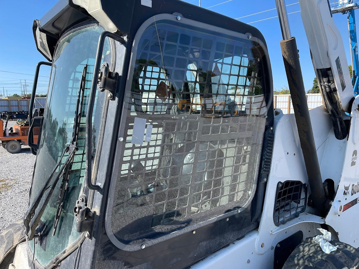 Bobcat M Series skid steer cab showing polycarbonate side window installed in door frame, outdoor yard setting