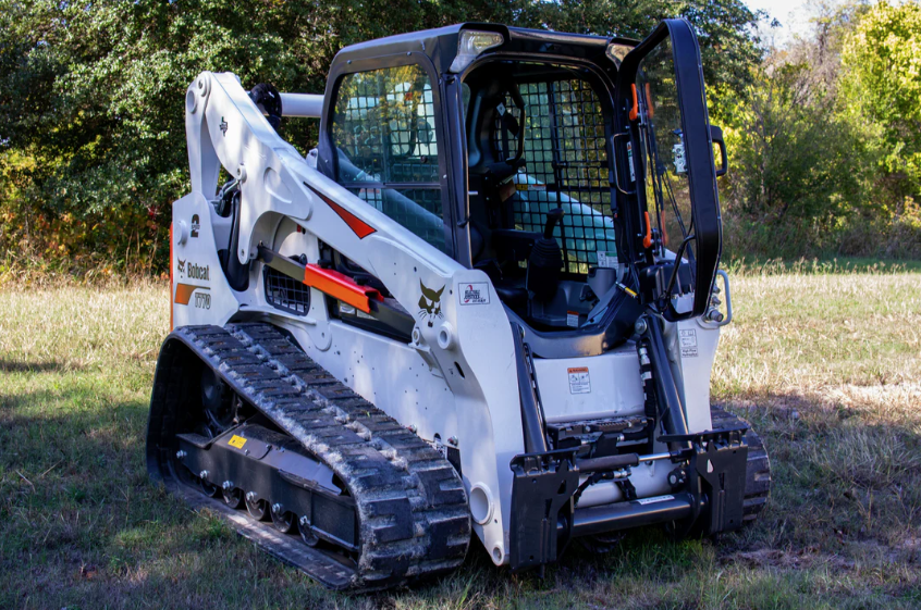 Bobcat M Series T770 compact track loader with open forestry door, side-rear view in wooded outdoor setting