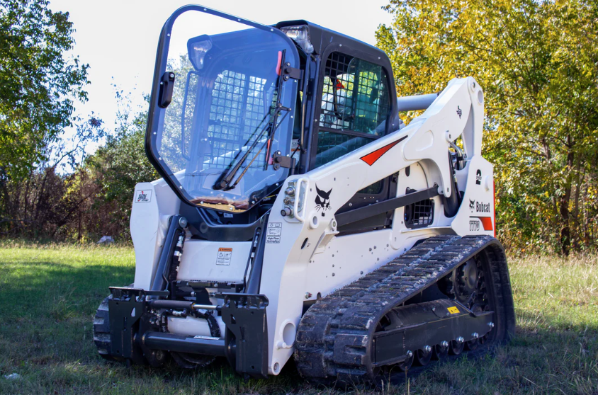Bobcat M Series compact track loader with forestry door installed, front-side view outdoors in wooded setting