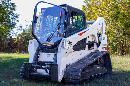 Bobcat M Series compact track loader with forestry door installed, front-side view outdoors in wooded setting