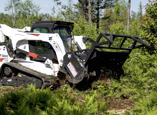 Bobcat M Series compact track loader with forestry mulcher attachment clearing thick vegetation in wooded area