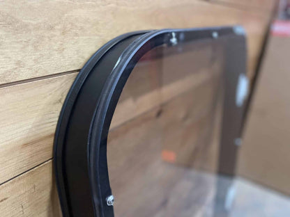 Close-up of Bobcat M Series windshield frame corner showing tinted polycarbonate panel seated in steel channel with rubber gasket