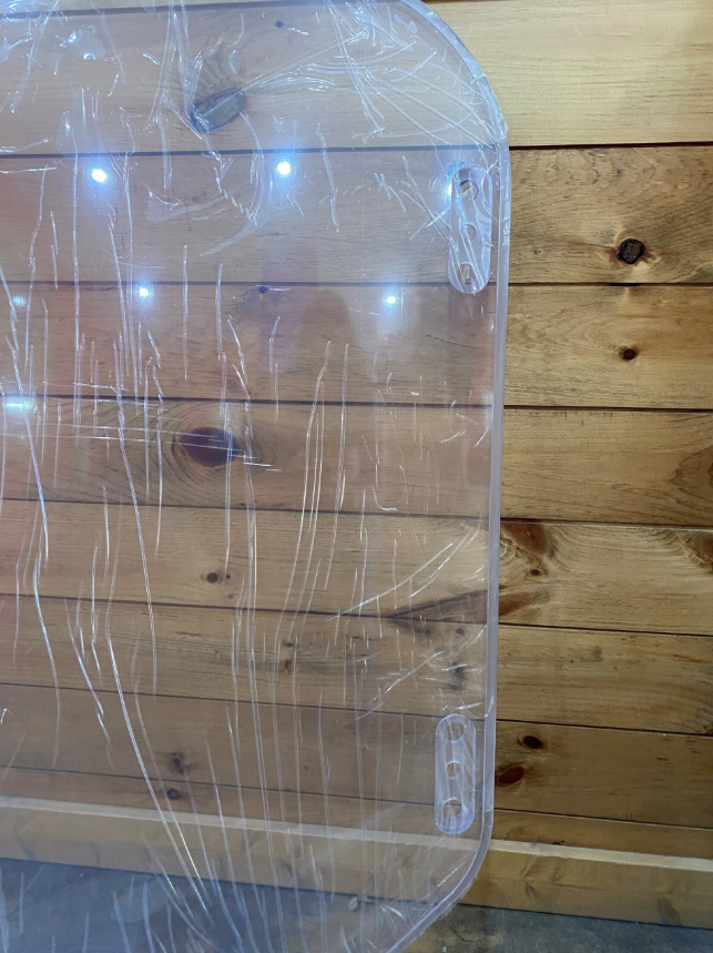 Bobcat M Series clear polycarbonate windshield, close-up of upper corner showing protective film and mounting bracket