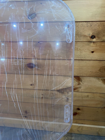 Bobcat M Series clear polycarbonate windshield, close-up of upper corner showing protective film and mounting bracket