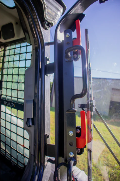 Bobcat R Series door frame close-up showing red lever latch and door handle hardware installed on skid steer