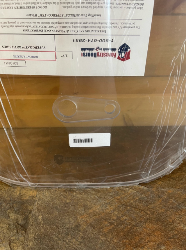 Close-up of Bobcat R Series polycarbonate windshield showing milled edge and panel thickness