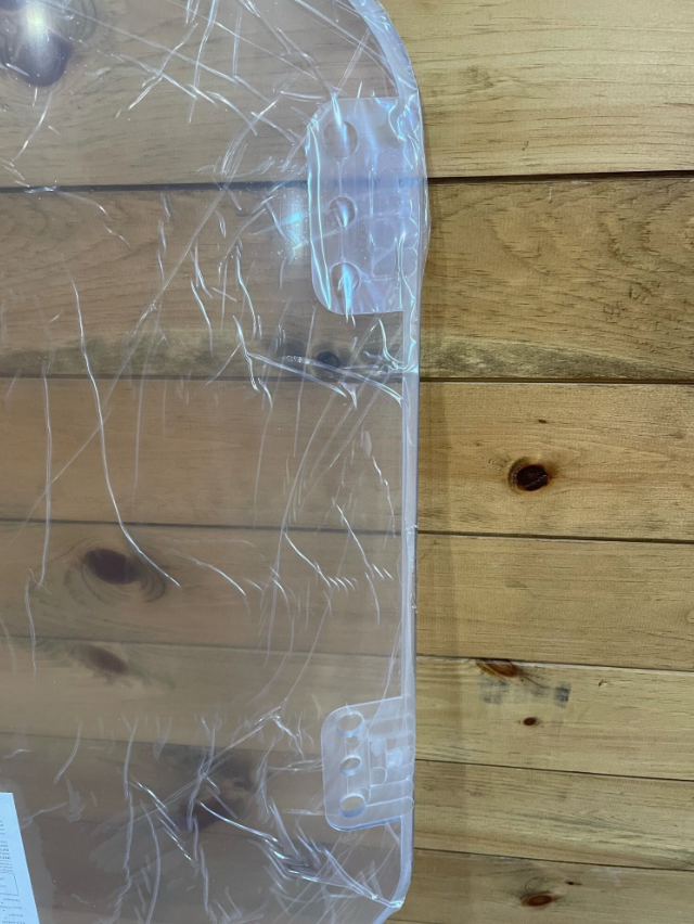 Top corner of Bobcat R Series polycarbonate windshield showing mounting hardware and clear panel