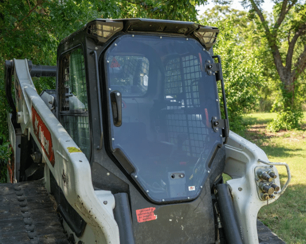 Compact track loader with tinted polycarbonate windshield installed, working outdoors