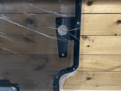 Close-up of Case/New Holland forestry door black frame corner showing bolt hole and tinted polycarbonate panel edge