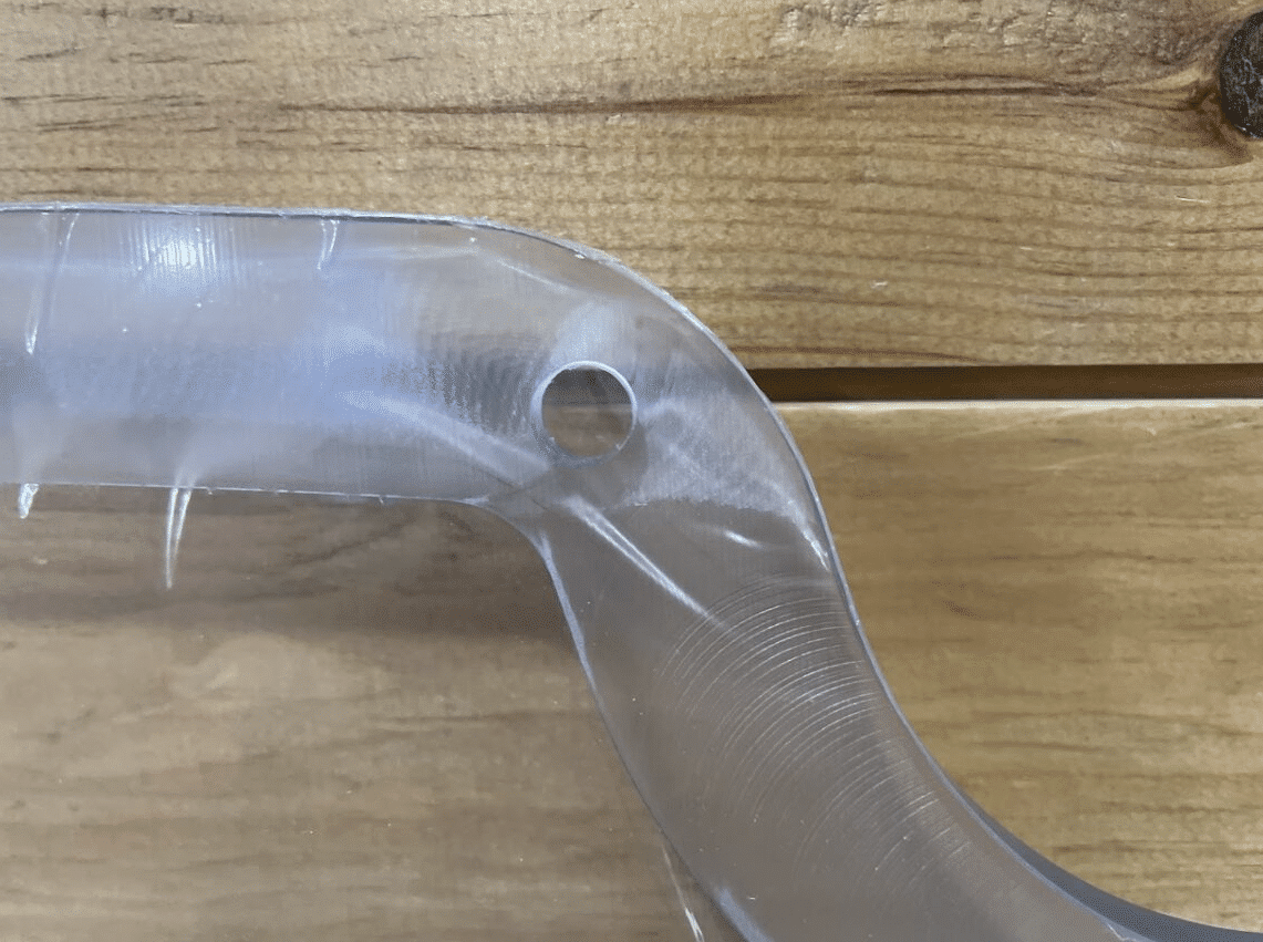Extreme close-up of Case/New Holland forestry door polycarbonate curved corner showing precision milled edge and bolt hole