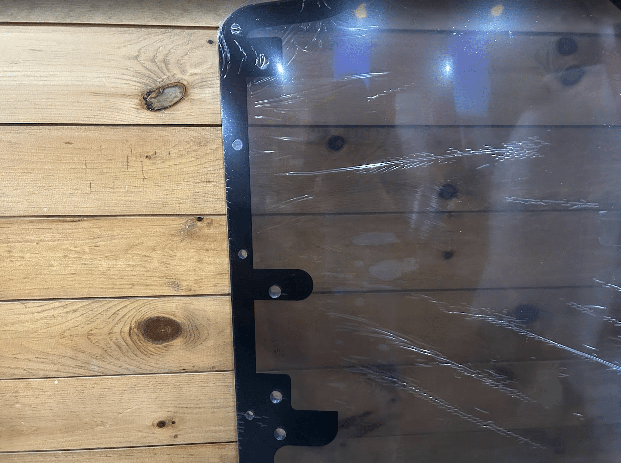 Top corner of Case/New Holland tinted polycarbonate forestry door showing black metal frame and corner bolt holes