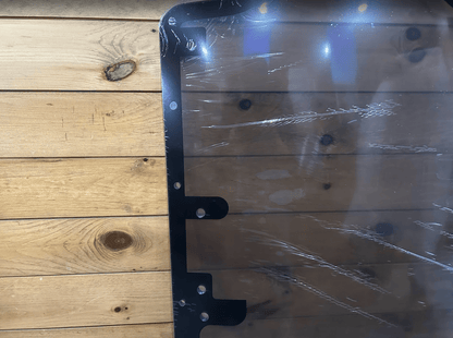 Top corner of Case/New Holland tinted polycarbonate forestry door showing black metal frame and corner bolt holes