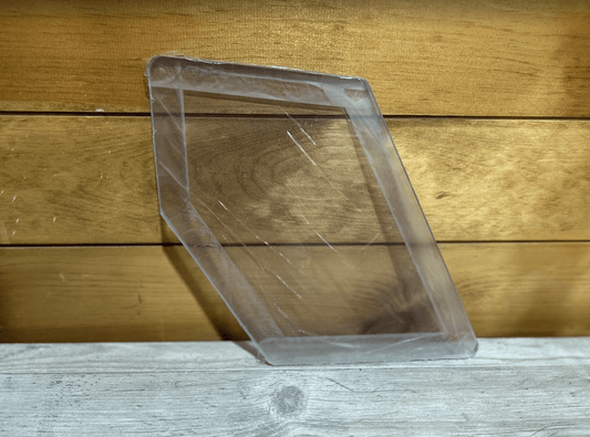 Clear polycarbonate Case and New Holland skid steer kick window leaning against a wood plank surface