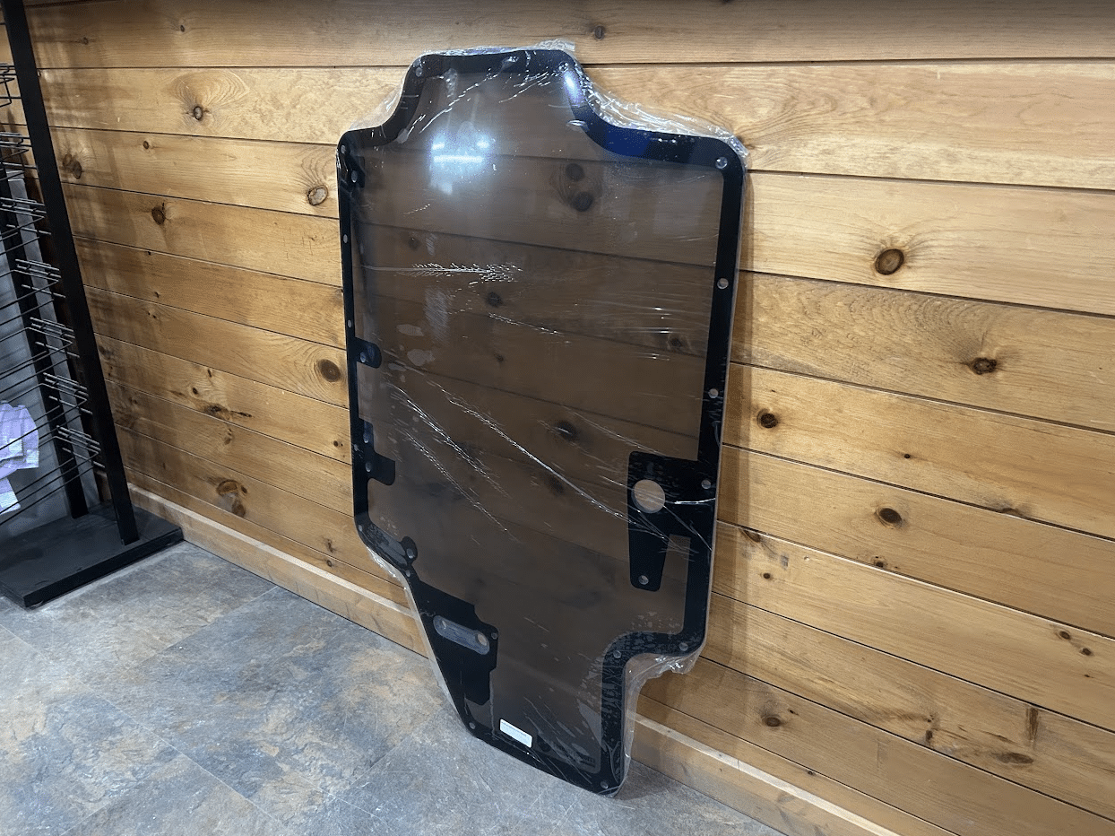 Case/New Holland SR/TR/SV/TV Series tinted polycarbonate forestry door leaning against wall, front angle showing all bolt holes