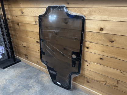 Case/New Holland SR/TR/SV/TV Series tinted polycarbonate forestry door leaning against wall, front angle showing all bolt holes