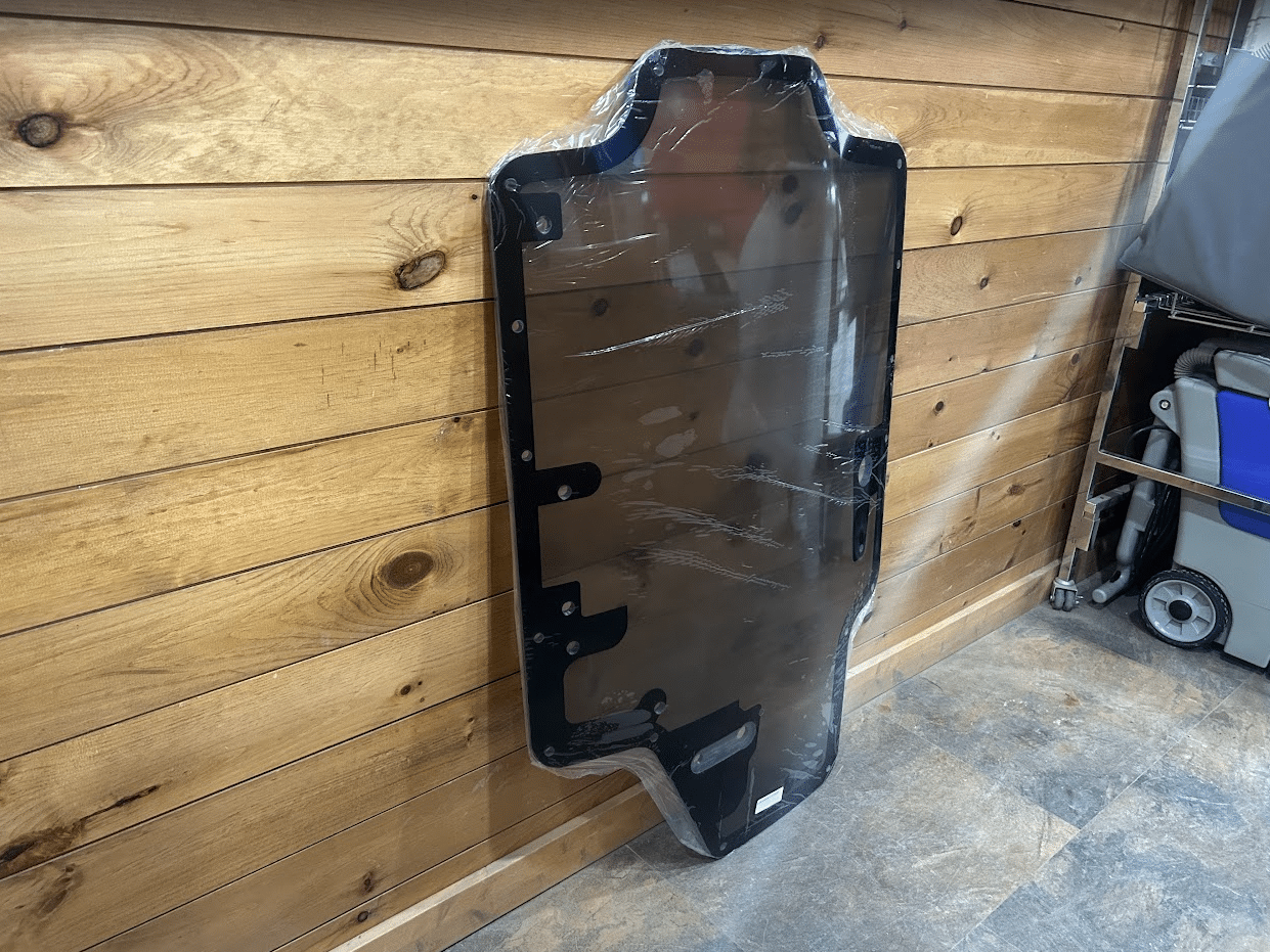 Case/New Holland tinted polycarbonate forestry door standing upright in garage showing full panel with black frame and wiper bracket
