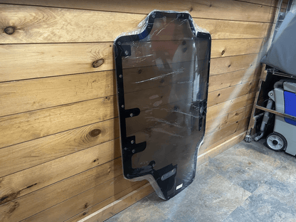 Case/New Holland tinted polycarbonate forestry door standing upright in garage showing full panel with black frame and wiper bracket