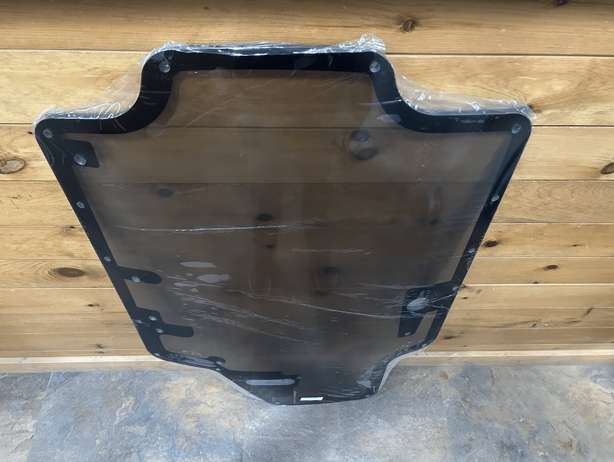 Case/New Holland SR/TR/SV/TV Series tinted polycarbonate forestry door with black rubber frame, full view against wood wall
