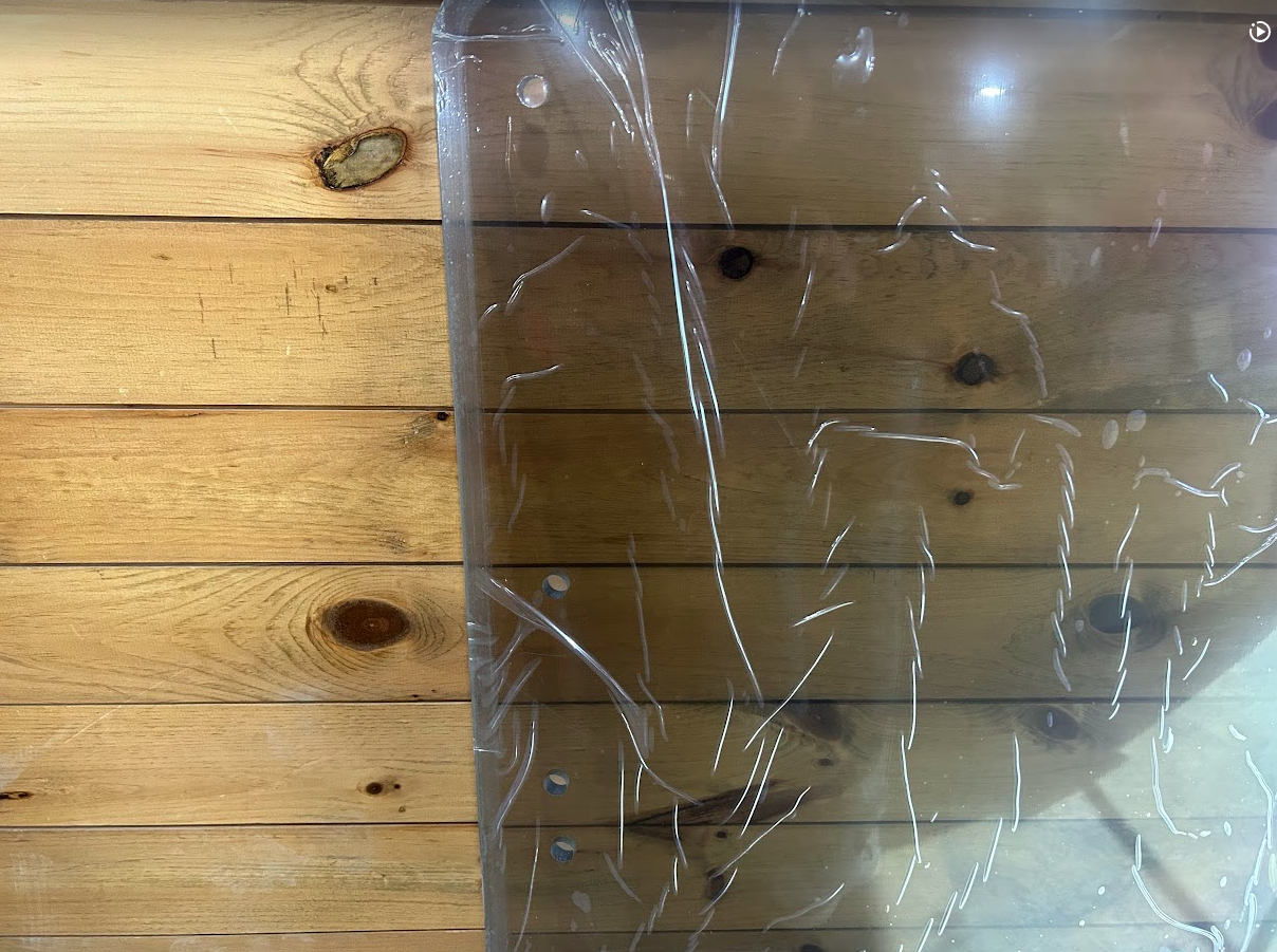 Close-up of clear polycarbonate windshield surface with protective film for Case SR TR SV TV Series skid steer, showing material clarity