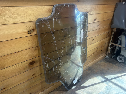 Case SR TR SV TV Series tinted polycarbonate windshield panel leaning against wooden wall, side angle showing panel thickness and shape