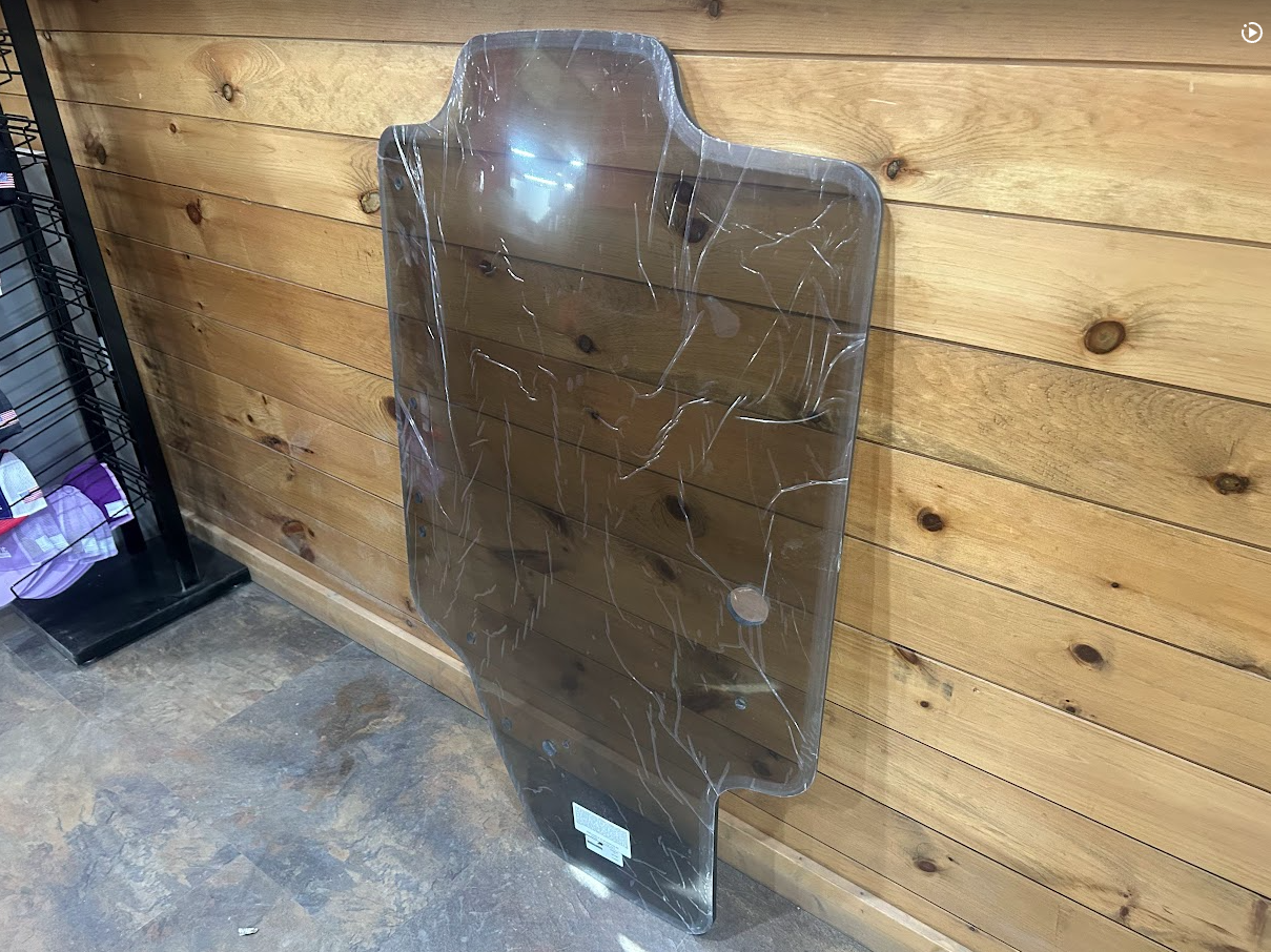 Case SR TR SV TV Series tinted polycarbonate windshield panel leaning against wooden wall in warehouse, single arm wiper style