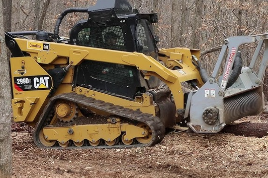 Caterpillar 299D2 compact track loader with mulcher attachment working in wooded area, compatible with tinted polycarbonate windshield replacement
