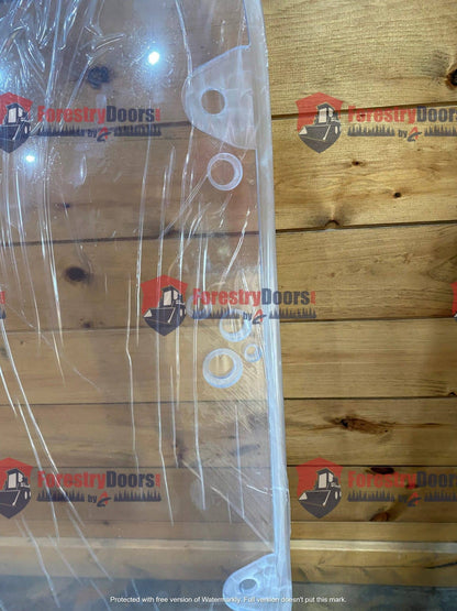 Close-up of Caterpillar D Series polycarbonate windshield upper section showing OEM mounting grommets with protective film on wooden background
