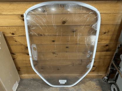 Clear polycarbonate Caterpillar skid steer windshield laid flat on a wood plank floor with protective film still on