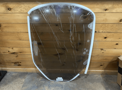 Clear polycarbonate Caterpillar skid steer windshield standing upright against a wood plank wall