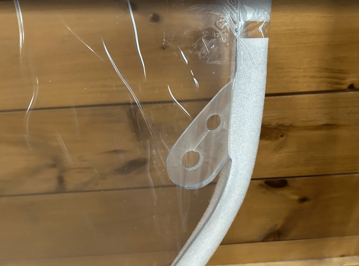 Close-up of the rounded corner and mounting holes on a clear polycarbonate skid steer windshield