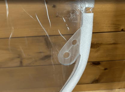 Close-up of the rounded corner and mounting holes on a clear polycarbonate skid steer windshield