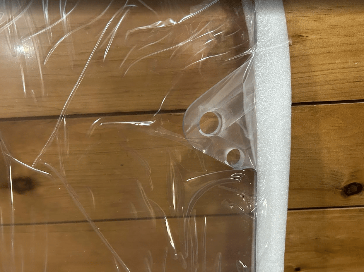 Close-up of two mounting holes near the corner of a clear polycarbonate skid steer windshield