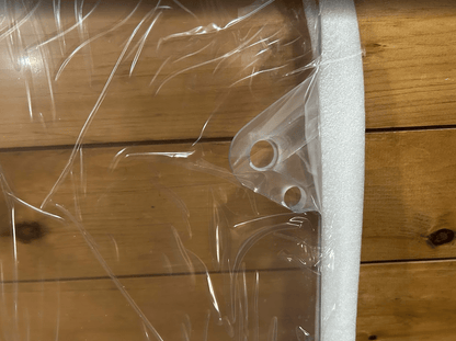 Close-up of two mounting holes near the corner of a clear polycarbonate skid steer windshield