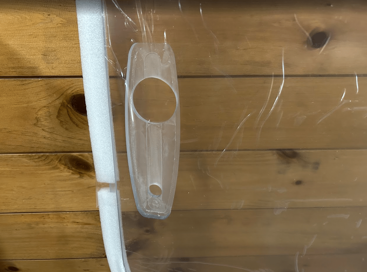 Close-up of a mounting hole and foam-padded edge on a clear polycarbonate skid steer windshield