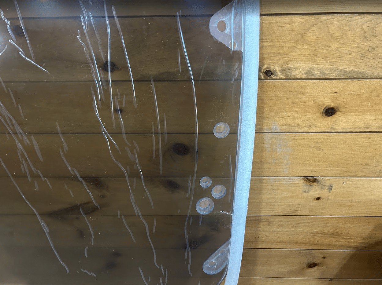 Close-up of multiple mounting holes along the edge of a tinted polycarbonate skid steer windshield
