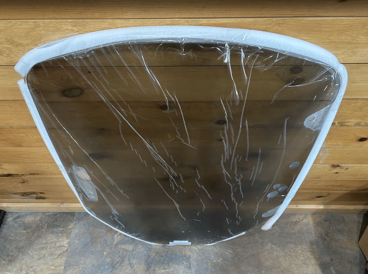 Tinted polycarbonate Caterpillar skid steer windshield standing against a wood plank wall, viewed at an angle