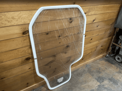 Gehl R and RT series clear polycarbonate windshield standing upright against a wooden wall